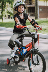 Adorable little girl in safety helmet riding bicycle outdoors