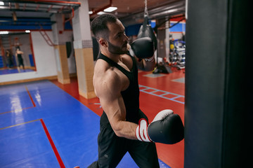 young muscular guy hitting punch bag at sport club. close up photo.hobby, interest