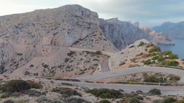 A panning view of cap formentor with  zic zac narrow roads, surrounded by two imposing filmy cliffs with charming clear blue water, shining sky, along the coast of the Mediterranean. mallorca