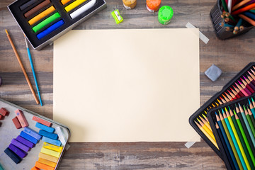 Flat lay top view of art workplace, wooden table with colored pencils, paper and crayon pastel...