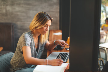 Young woman writing a note with pen with laptop on table at a coffee shop.