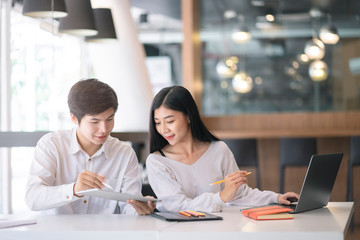 Young Asian couple or college student using digital tablet and laptop computer notebook work together at coffee shop or university campus.