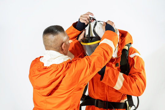 Firefighter Or Fireman In Fire Suit Helping Friend Wearing Fire Protection Suit In Safety Emergency Fire Training Class Isolated White Background. Safety Officer Fireman Preparing For Rescue Concept.