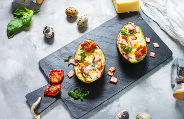 Keto diet - Avocado with ham, quail eggs, cheese on concrete background