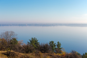 Reservoir from steep shore overgrown with trees in morning haze