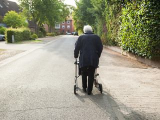 Very old lady walking alone in sunny street with walker, walking frame