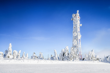 Frozen television or cellular tower in heavy snow near ski center. Telecommunication towers with dish and mobile antenna against blue sky in winter mountains. - Powered by Adobe