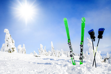 Skis in snow with gloves copy space. Green skis standing in heavy snowy winter and forest frozen trees or mountains in background. Winters holiday skiing concept.