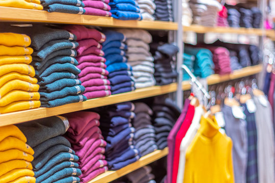 Warm clothing neatly folded on a shelf. A row of colorful jumpers, cardigans, sweatshirts, sweaters, hoodies in the showroom or store.