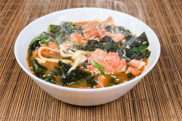 Bowl of miso salmon soup on bamboo table mat closeup