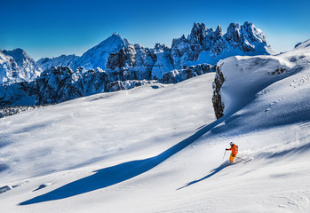 Skier in deep snow makes a snow wave behind him. Free rider going fast in fresh snowy slope high in winter mountains.