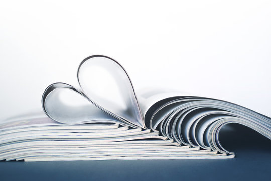 Pages of the journal, curved into heart shape, selective focus. Stack of magazines on the table.