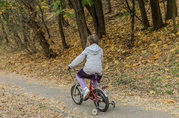 Naklejka premium Little happy girl child rides a bicycle in the autumn forest
