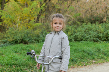 Little happy girl child rides a bicycle in the autumn forest