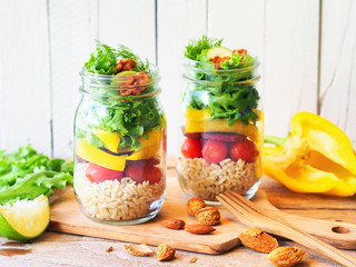 Vegan salad jar with green oak, yellow bell peppers beetroot, cherry tomato, and brown rice on a rustic chopping board for dietary food or light meal concept.