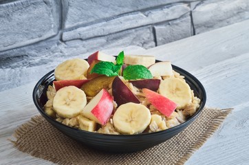 Delicious sweet healthy breakfast. Oatmeal with apples, bananas, honey and plums.