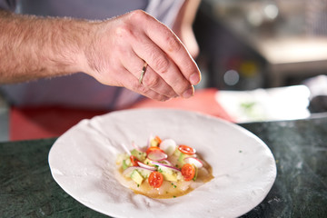 The chef serves the dish Tartar from scallop with avocado, cherry tomatoes, radishes and onion. Dish in the restaurant from raw seafood.