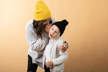 A young and energetic mother hugs and kisses her son on an orange background