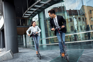 Two smiling business people driving electric scooter in front of modern business building going on work. © Zoran Zeremski