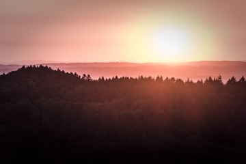 Wonderful magic sunshine over a german forest. Sunrise or sundown at the horizon of a large forest in Germany in europe. A very idyllic and magical scene with beautiful colors