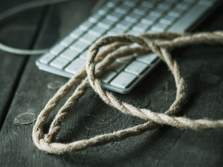 Rope and keyboard on a rough wood table. Concept of hacker attack, data security, harassment, depression or loneliness.