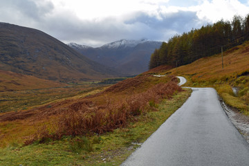 Single track road through Glen Etive, Scottish Highlands with snow capped mountains in background