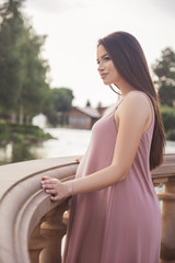 Sexy brunette pregnant woman in park. Summer day, sunset