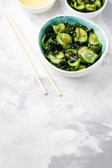 Traditional Japanese dish tasty appetizing seaweed salad served with cucumber in bowl on light blue background.Organic natural product.Raw,vegan,vegetarian food.Vertical with copy space.