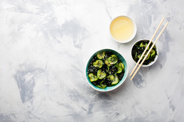 Traditional Japanese tasty appetizing seaweed salad served with cucumber in bowl on light blue...