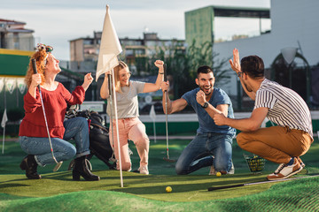 Obraz premium Group of smiling friends enjoying together playing mini golf in the city.