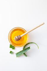 Aloe Vera leaves and fresh honey in bowl on white background