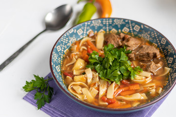 Eastern dish Lagman. Noodles, beef, blue, pepper, tomatoes. Hearty dish. Top decorated with parsley and cilantro. On a light background. Copy space.
