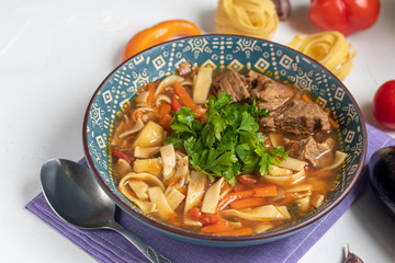 Eastern dish Lagman. Noodles, beef, blue, pepper, tomatoes. Hearty dish. Top decorated with parsley and cilantro. On a light background. Copy space.