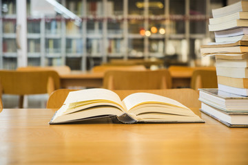 Old textbook are open and stack books placed on a wooden table on blurred bookshelf in library room background, reading for learning about thinking technique and how to concept