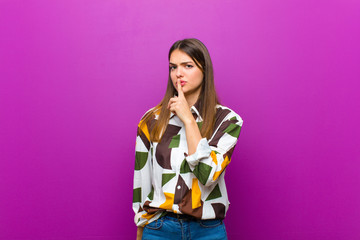 young pretty woman asking for silence and quiet, gesturing with finger in front of mouth, saying...