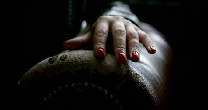 Close-up of a woman's hand, which with red nails, she strokes the arm of a leather sofa.