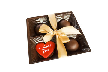 Four round chocolate candies in a plastic square box tied with a yellow ribbon with a bow and small red heart with a love inscription on a white background