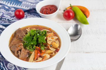 Eastern dish Lagman. Noodles, beef, blue, pepper, tomatoes. Hearty dish. Top decorated with parsley and cilantro. On a light background. Copy space.