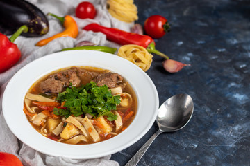 Eastern dish Lagman. Noodles, beef, blue, pepper, tomatoes. Hearty dish. Top decorated with parsley and cilantro. On a dark background. Copy space. 