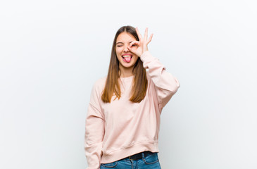 young pretty woman smiling happily with funny face, joking and looking through peephole, spying on...
