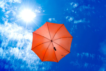 Orange umbrella in bottom view for protect skin from the sun, high uv on the blue summer sky with white fluffy clouds. Photo from window on the airplane.
