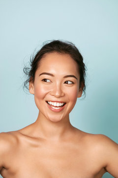 Beauty face. Smiling asian woman with perfect skin portrait. Beautiful happy girl model with healthy glowing facial skin and natural makeup and white smile on blue background at studio