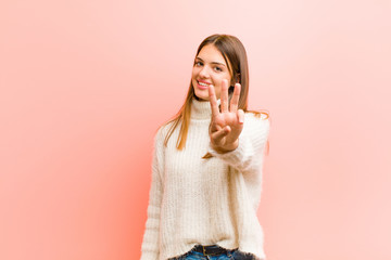 young pretty woman smiling and looking friendly, showing number three or third with hand forward,...