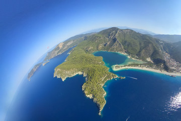 Paragliding in the sky. Paraglider tandem flying over the sea with blue water and mountains in bright sunny day. Aerial view of paraglider and Blue Lagoon in Oludeniz, Turkey. 