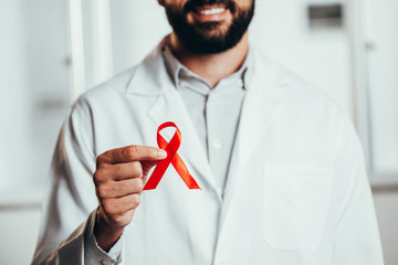 Red ribbon for HIV illness awareness in doctor's hand, 1 December World AIDS Day concept.