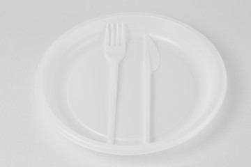 White plastic fork and knife lie in a plate on a white background