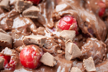 Background of chocolate dough with pieces of milk chocolate and frozen cherries
