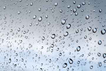 Drops of water on the glass window against a blurred blue and gray sky background on a rainy autumn day. Selective focus