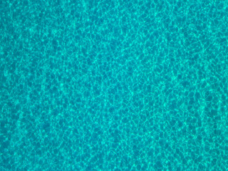 Aerial view of a sandy seabed, crystal clear blue water, reflections of the sun cause ripples on the sea surface. Texture and background. Pool