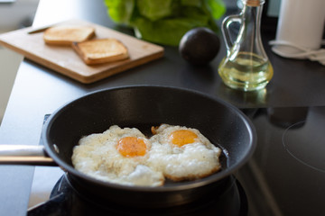 Preparing early morning eggs breakfast on modern induction stove in home kitchen.